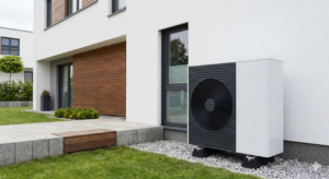 Venkovní jednotka moderního tepelného čerpadla vzduch-voda instalovaná čistě na štěrkovém loži vedle současného rodinného domu, připravená pro úsporné vytápění.